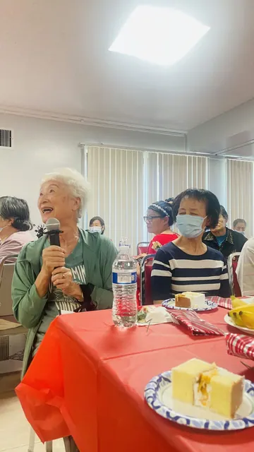 生日會上長者手持麥克風發言,桌上擺著蛋糕