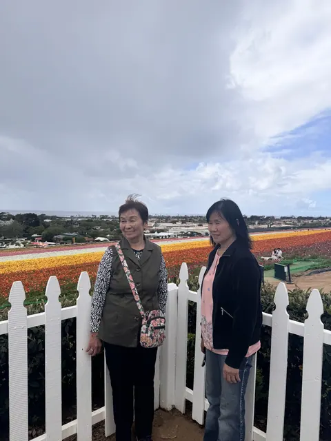 兩位住戶在白色圍欄前留影,身後是繽紛花田與海岸景色