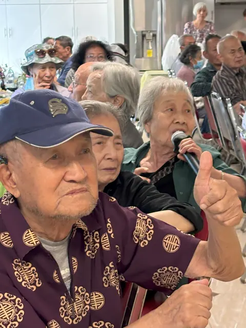 住戶手持麥克風分享友誼故事,身旁的住戶豎起大拇指